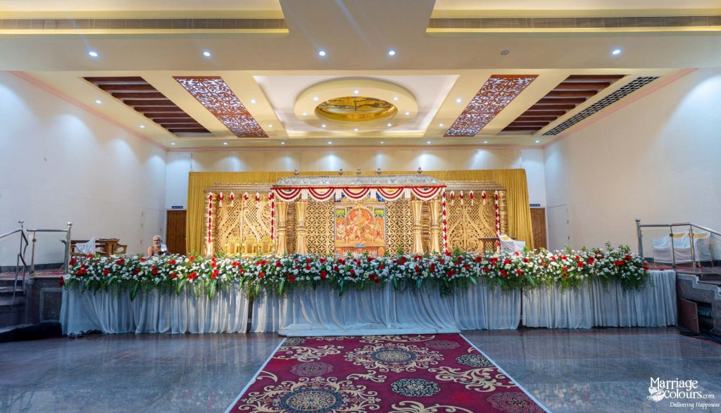 Grand wedding stage featuring intricate golden carvings, an elaborate floral border, and a red carpet.
