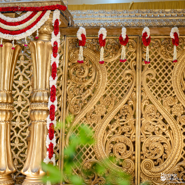 Close-up of traditional wedding stage backdrop with ornate golden carved panels and red and white flower garlands.