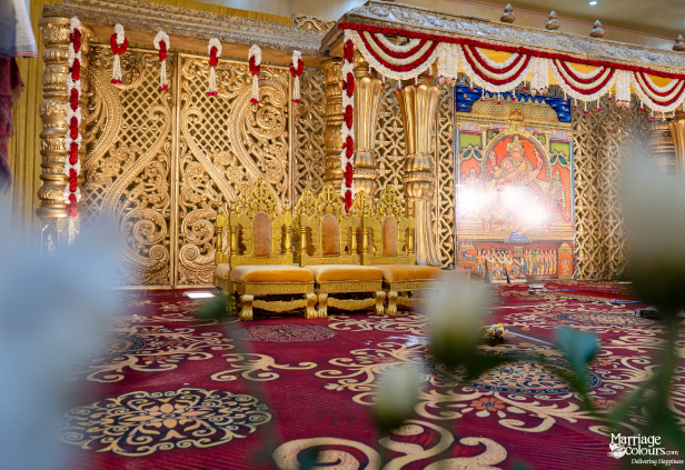 Grand wedding stage with a golden sofa, intricate gold carvings, and a central Hindu deity painting.