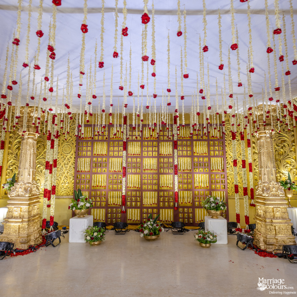 Grand indoor stage with a golden lattice backdrop, towering gold pillars, and abundant hanging red and white flower garlands.