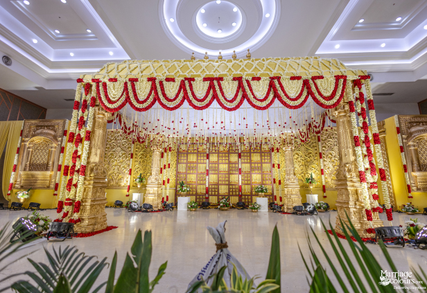 Grand wedding stage with a golden mandap, towering floral pillars, and a gold lattice backdrop.