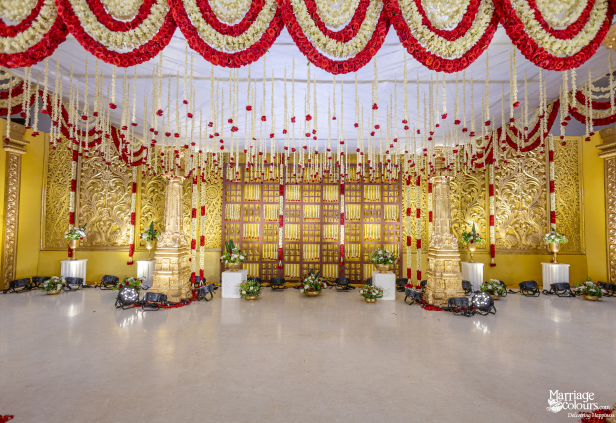 Grand traditional stage with a golden lattice backdrop, towering gold pillars, and abundant hanging red and white flower garlands.