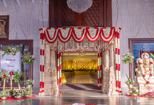 Wedding entrance arch with red and white garlands, golden pillars, a welcome sign, and a Ganesha statue.