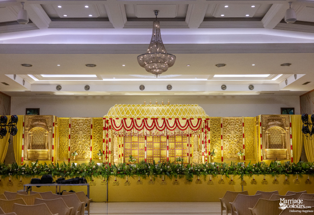 Grand yellow wedding stage with a gold mandap, red and white garlands, and a lush floral border.