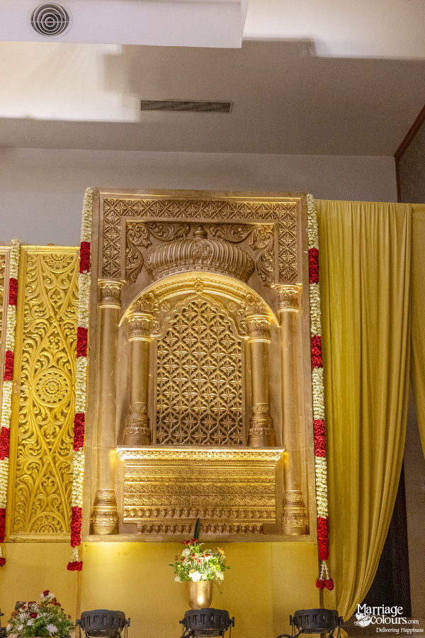 Traditional wedding stage corner with a golden carved niche, red and white garlands, and yellow drapes.