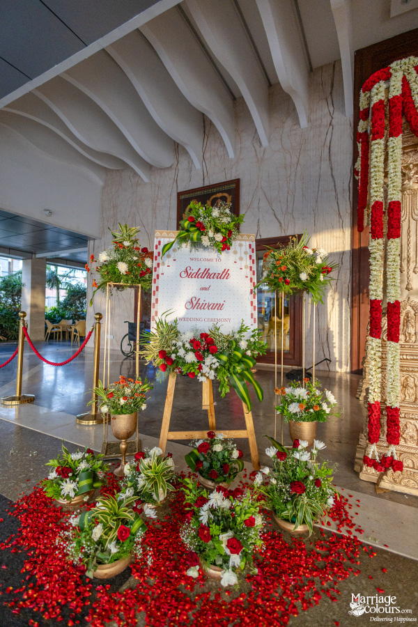 Wedding welcome sign for Siddhaarth and Shivani on an easel, surrounded by red rose petals and floral arrangements.