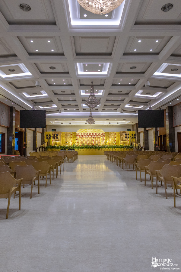 Grand wedding hall interior with a long aisle of empty chairs leading to a brightly lit, golden stage.