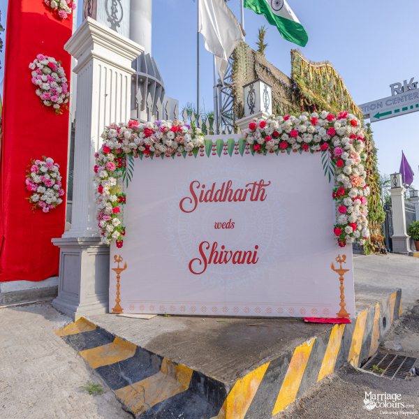 Wedding welcome sign for Siddharth and Shivani, decorated with pink and white flowers and standing near a red pillar.