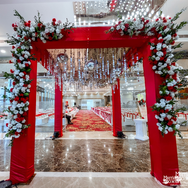 Red wedding entrance arch decorated with white and red flowers and hanging crystal strings.