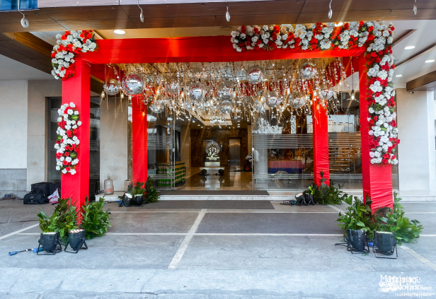Red wedding entrance arch decorated with white and red flowers and hanging disco balls.