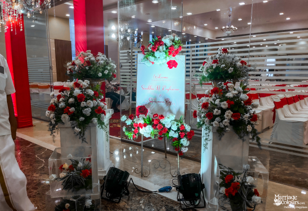 Wedding stage with cream drapery backdrop, a white arch, chandelier, and red and white flowers.