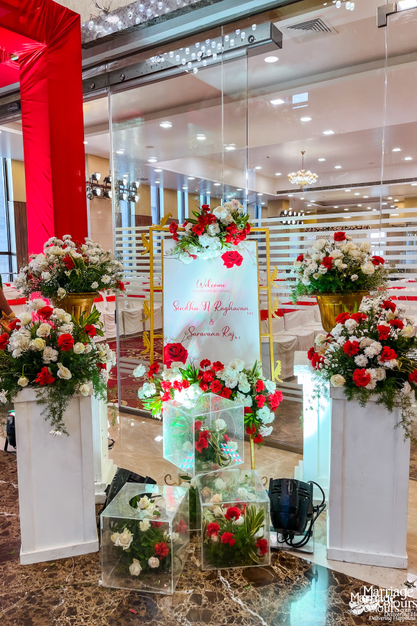 Wedding welcome sign for Sindhu N Raghavan and Suwarna Raj, surrounded by red and white flowers.