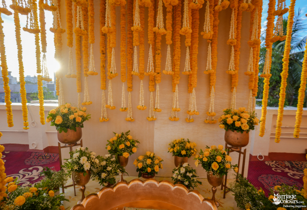 Yellow marigold and jasmine garlands hanging from a sunlit backdrop with yellow rose bouquets.