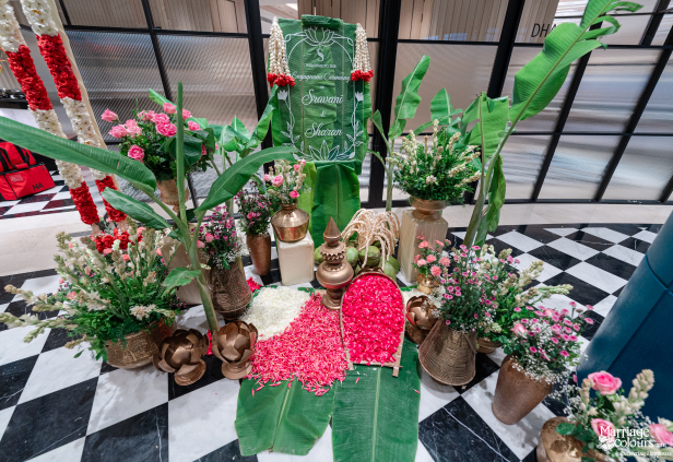 Lush engagement ceremony decor on a checkered floor with banana leaves and pink floral arrangements.