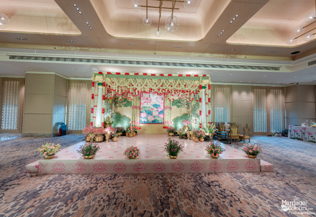 Wide shot of an elegant indoor wedding stage with a soft pink lotus theme and floral arches.