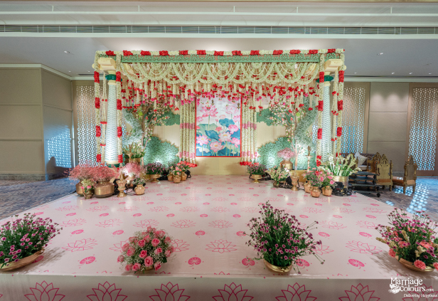 Wide shot of an elegant indoor wedding stage with a soft pink lotus theme and floral arches.