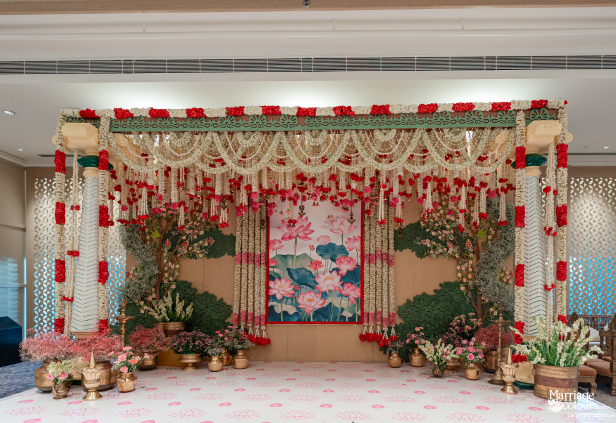 Intricate lotus-themed wedding stage with draping white and red floral garlands and greenery.