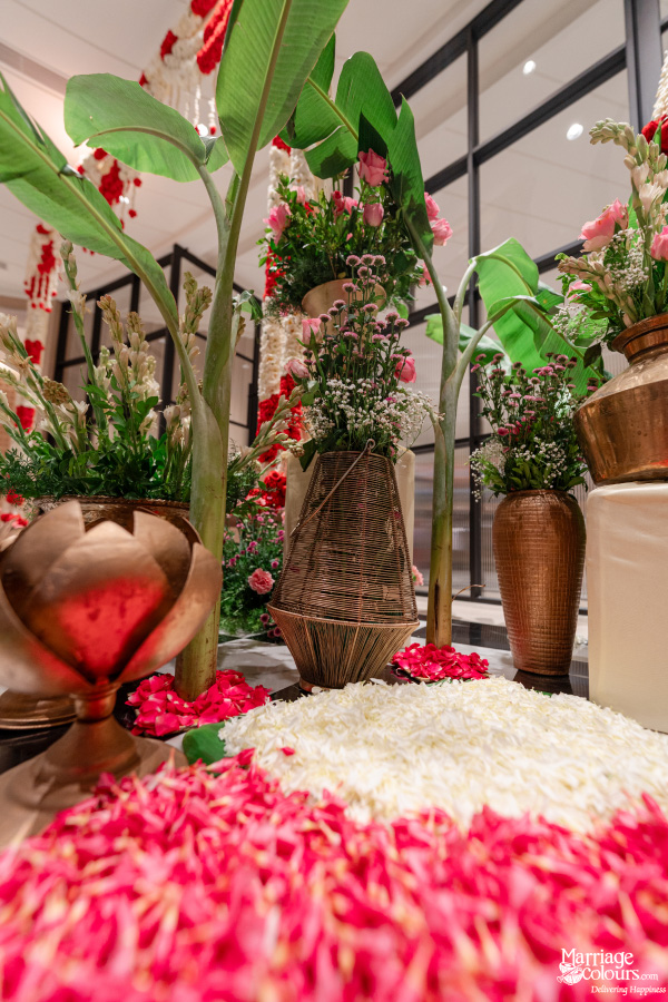 Vibrant wedding decor with mounds of red and white petals, brass vessels, and banana leaves.
