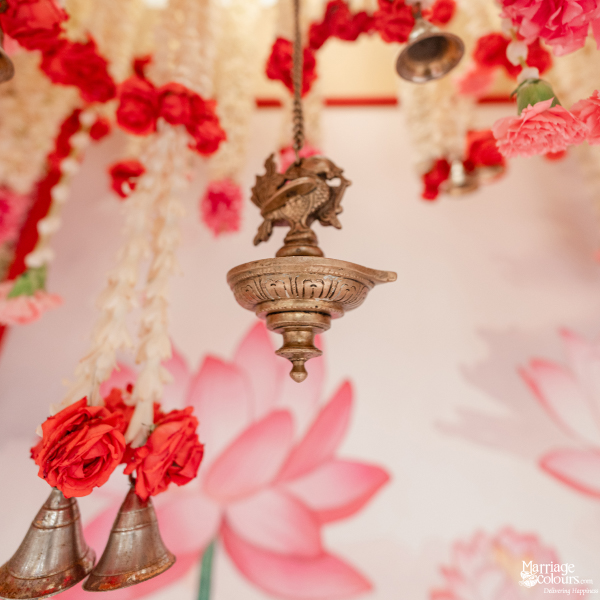 Hanging brass ritual lamp and bells amidst draping red and white wedding floral garlands.