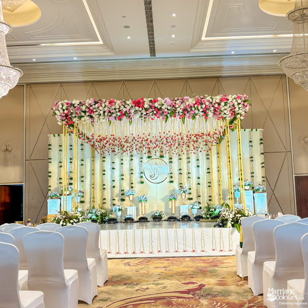 Elegant ballroom stage with a gold backdrop, pink and white flower top, and white chair covers.