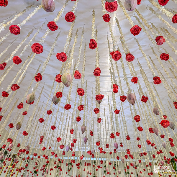 Close-up view of a ceiling canopy decorated with numerous hanging red roses and white jasmine strings.