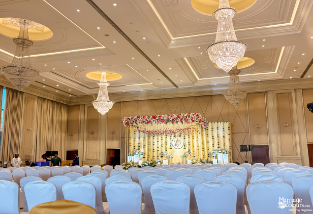 Wide-angle view of a large, luxurious wedding hall with crystal chandeliers and floral stage decor.