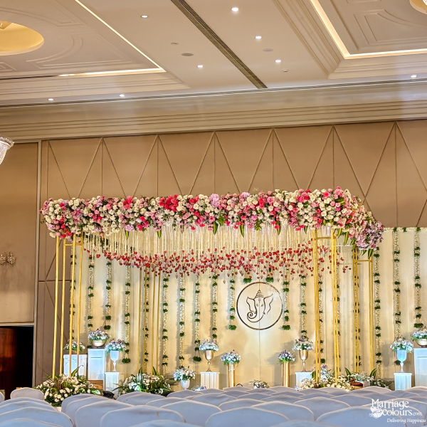 Elegant wedding stage with a massive pink and white floral canopy and a central Ganesha logo.