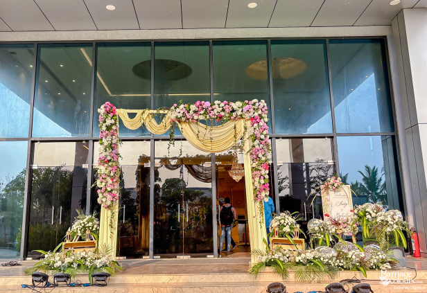 Modern building entrance decorated with a pink, white, and yellow floral arch and soft yellow draping.