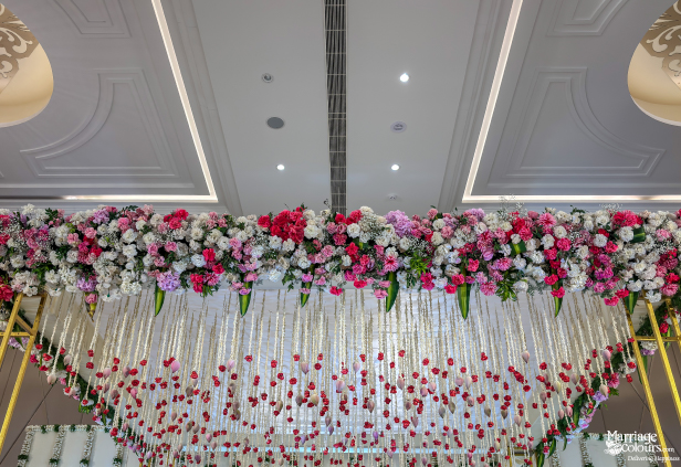 Close-up of a wedding stage ceiling decorated with a dense pink and white flower cluster and hanging red flowers.
