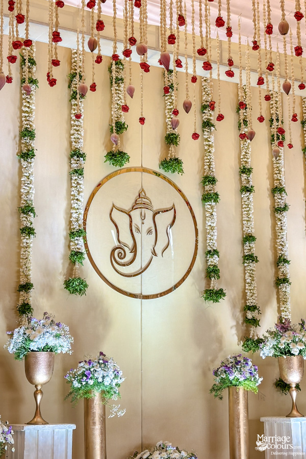 Elegant wedding or ceremony backdrop with Ganesha motif, long floral strings, and white and gold vases.