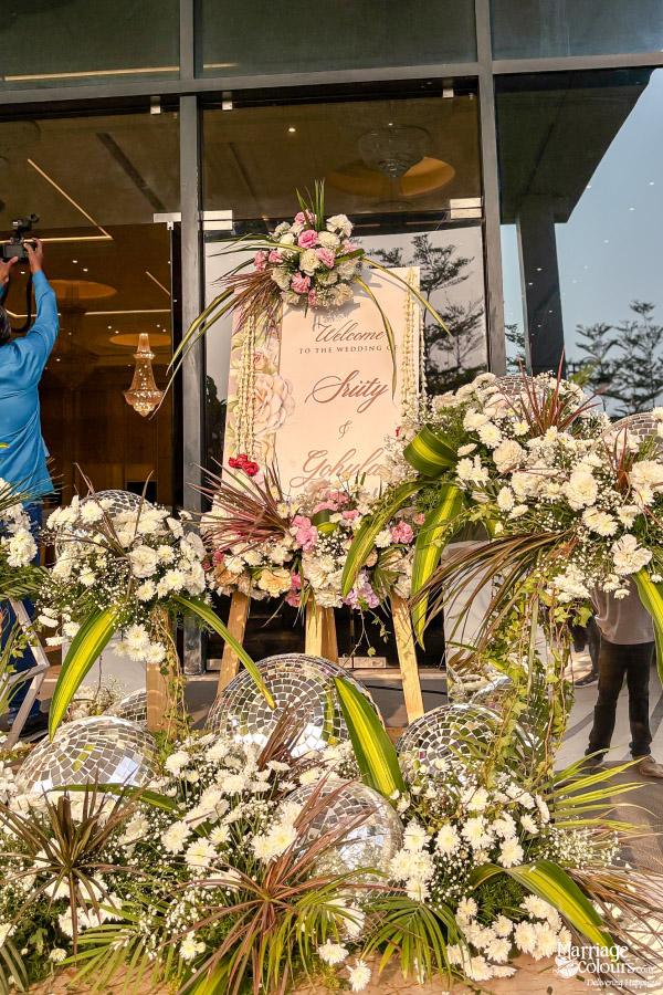 Elegant wedding welcome sign on an easel surrounded by white flowers, green foliage, and disco balls.