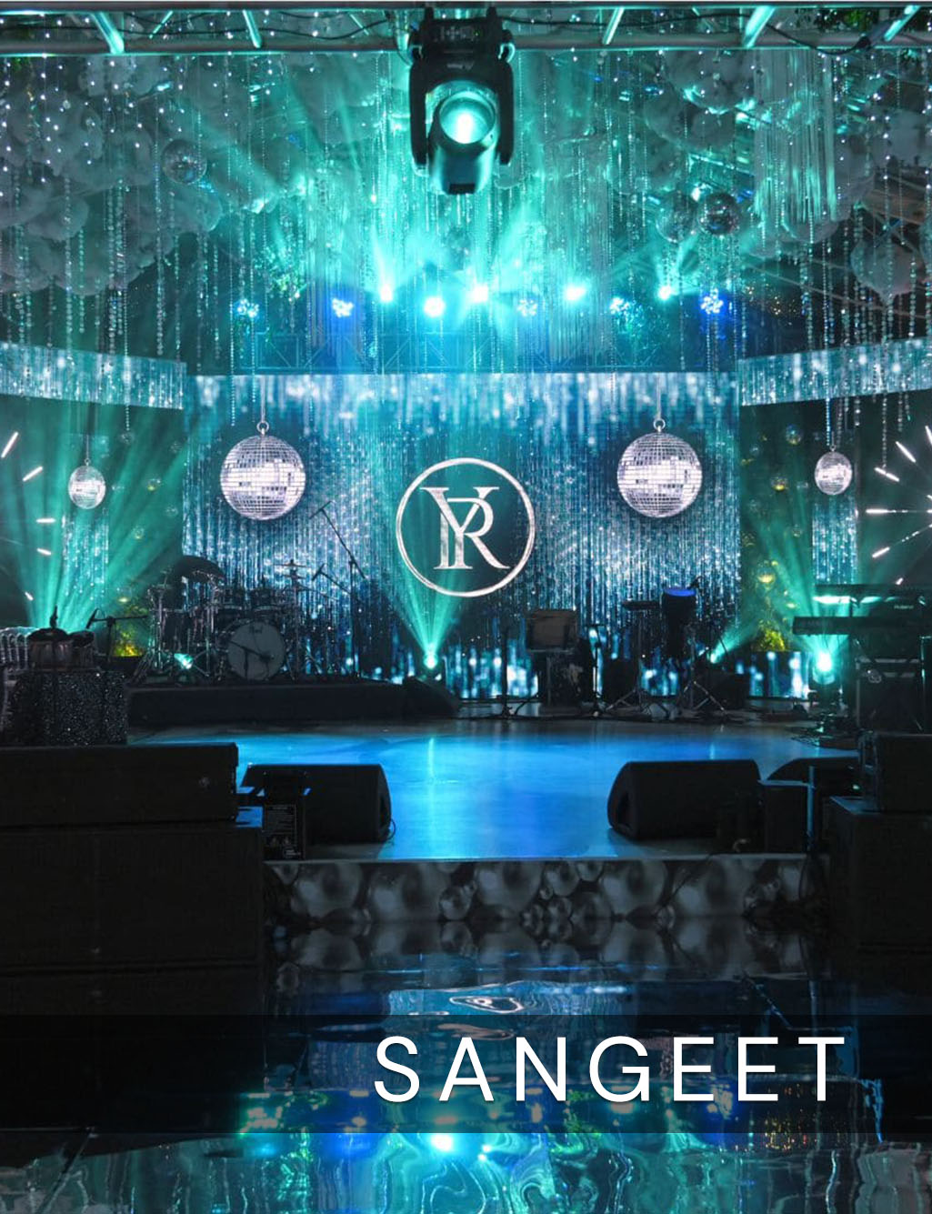 Disco Sangeet stage lit in icy blue and green, featuring hanging mirror balls and a large monogram