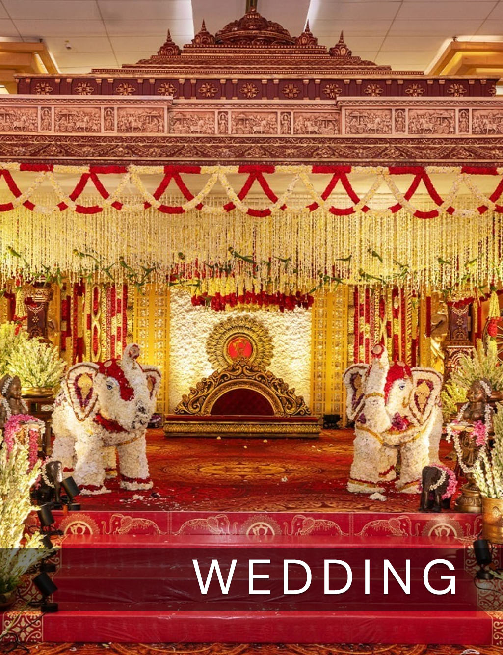 Traditional red and gold wedding mandap featuring a regal central throne and two intricately decorated floral elephants.
