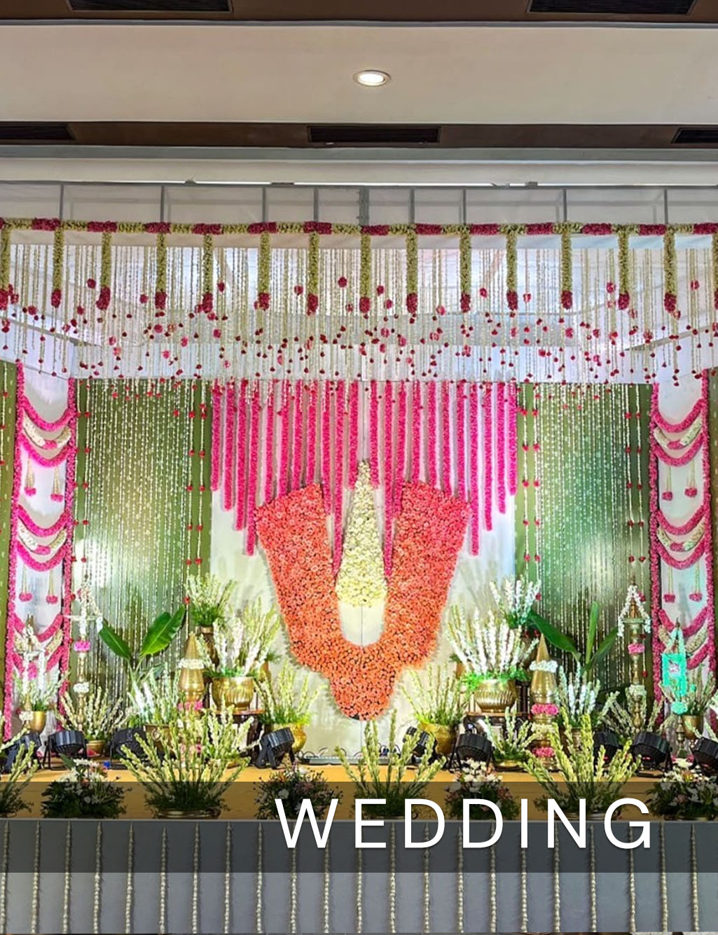 Vibrant wedding stage with pink and white floral hangings centered around a large orange and white flower motif.