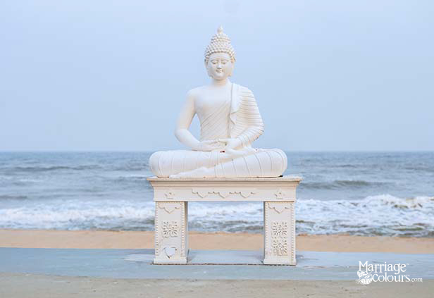 White Buddha statue on ornate pedestal at beach with ocean waves in background