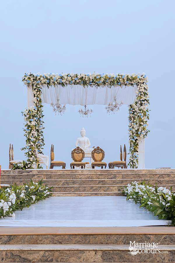 Outdoor wedding aisle with floral arch, Buddha statue, and couple’s photo and welcome sign on easels