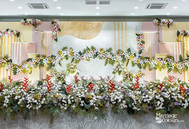 Close-up of elegant wedding stage floral decor with white daisies, red heliconia, and greenery against a gold leaf-patterned backdrop