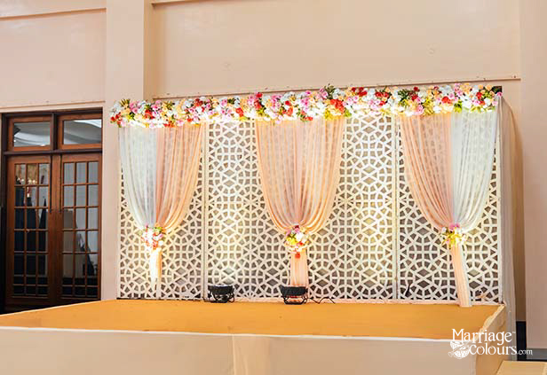 Indoor wedding stage decoration with floral drapes and lattice backdrop for reception or engagement ceremony