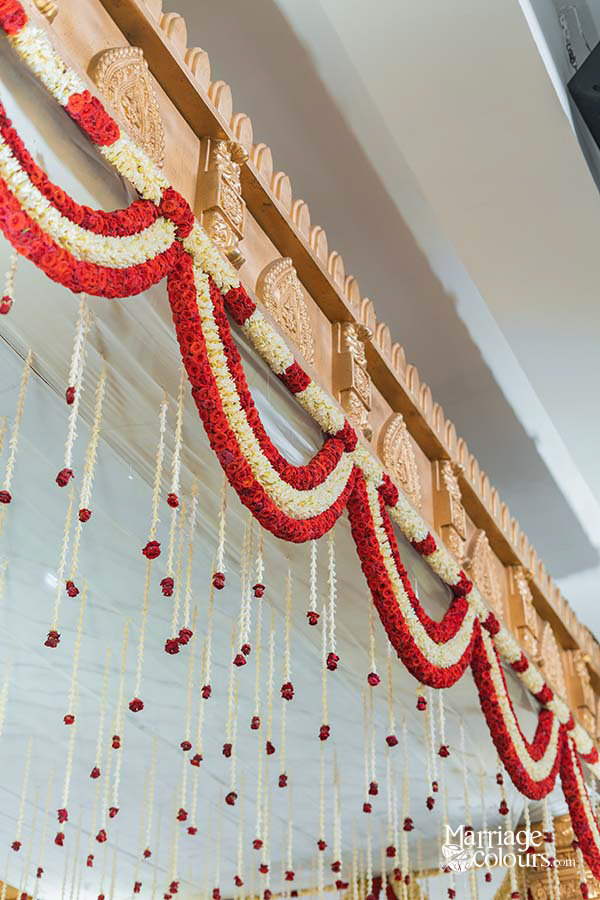 Close-up of red and white floral garlands draping over a wooden mandap frame