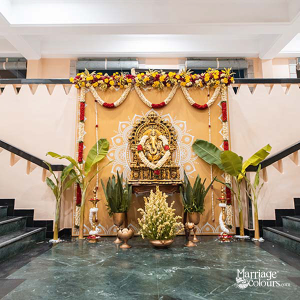 Traditional Indian wedding stage with Ganesha idol, floral garlands, and banana leaves on a marble floor.