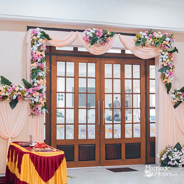 Wedding entrance doorway decorated with floral arches, pink drapes, and greenery in a banquet hall
