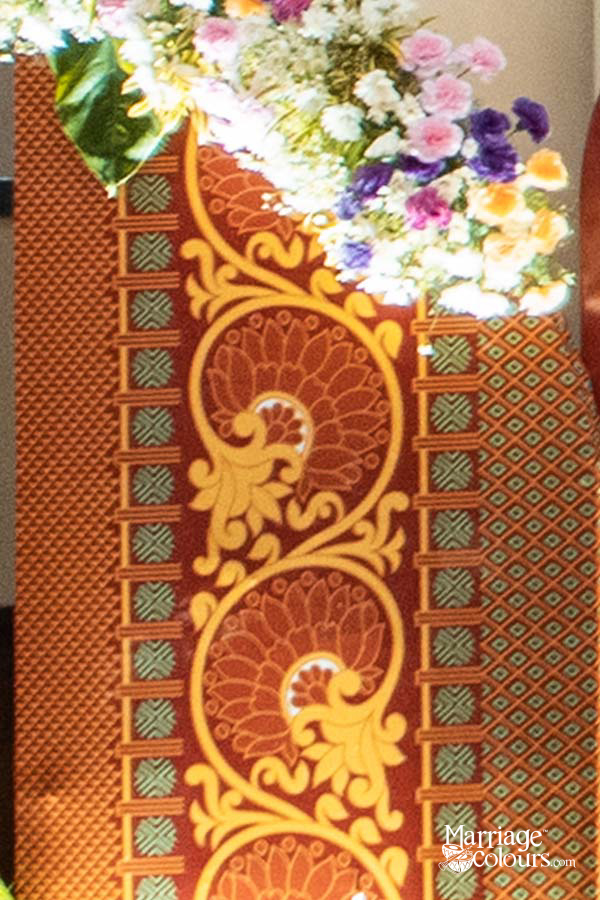 Close-up of ornate wedding welcome board with gold floral patterns, red textured background, and fresh pink, white, and purple flower arrangement
