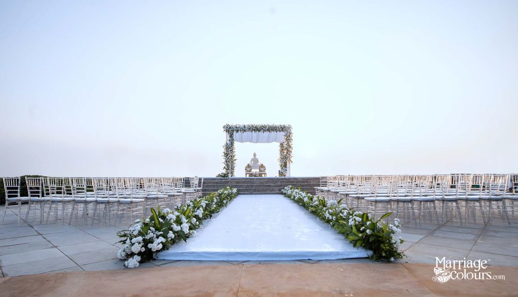 Elegant outdoor wedding ceremony setup with white aisle runner, floral arch, and Chiavari chairs at dusk