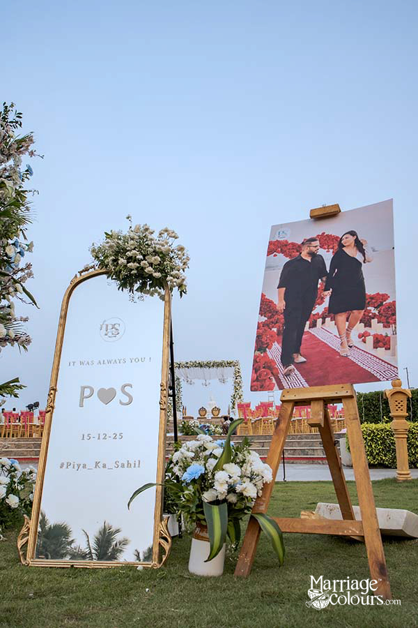 Wedding welcome display with gold-framed mirror and couple photo on easel, decorated with white flowers