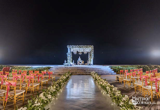 Nighttime outdoor wedding stage with illuminated floral arch, photo displays, and Buddha statue under spotlight