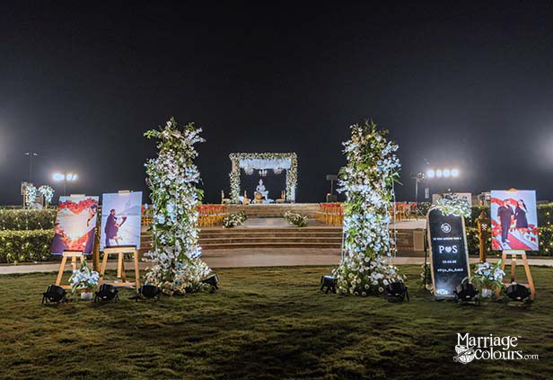 Evening wedding stage with Buddha statue under floral arch, flanked by pink-sashed chairs and white blooms