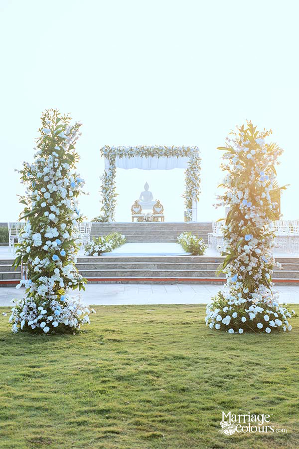 Outdoor wedding ceremony setup with floral arches and Buddha statue under soft sunlight