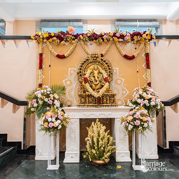 Traditional Indian wedding mandap decorated with flowers, draped fabric, and a golden deity idol in a banquet hall
