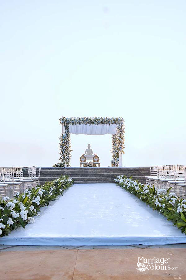 White wedding aisle leading to a floral arch with Buddha statue at the altar, surrounded by greenery