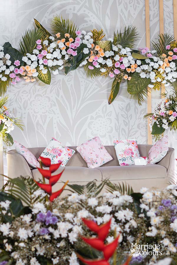 Close-up of wedding stage floral decor with white daisies, red heliconia, and greenery on a textured white backdrop